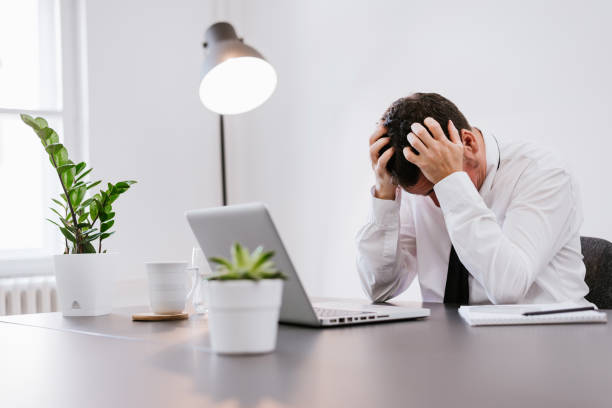 istock Frustrated elder businessman sitting on desk with hand on head in office. 697248826