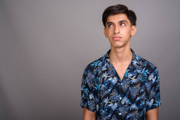 Studio shot of young Persian teenage boy wearing Hawaiian shirt against gray background Studio shot of young Persian teenage boy wearing Hawaiian shirt against gray background horizontal shot rolling eyes stock pictures, royalty-free photos & images