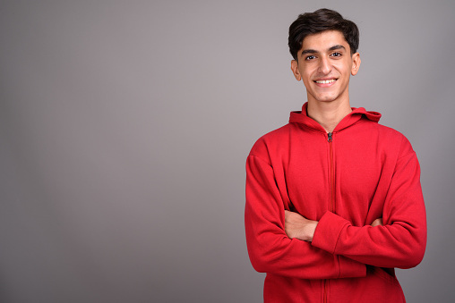 Studio shot of young Persian teenage boy wearing red jacket against gray background horizontal shot