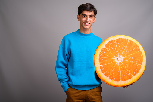 Studio shot of young Persian teenage boy wearing blue sweater against gray background horizontal shot