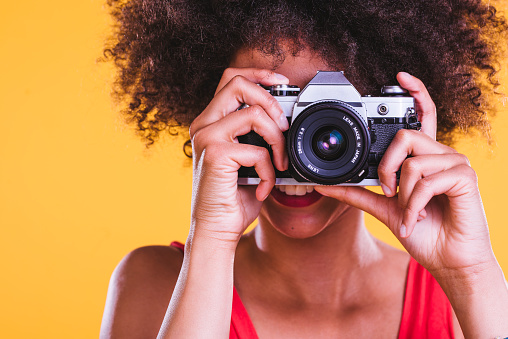 Young African-American woman standing and holding camera in her hands. She is taking photo.