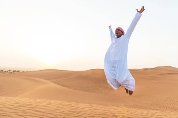 alegre jovem árabe saltando sobre as dunas de areia - travel adventure water oman - fotografias e filmes do acervo