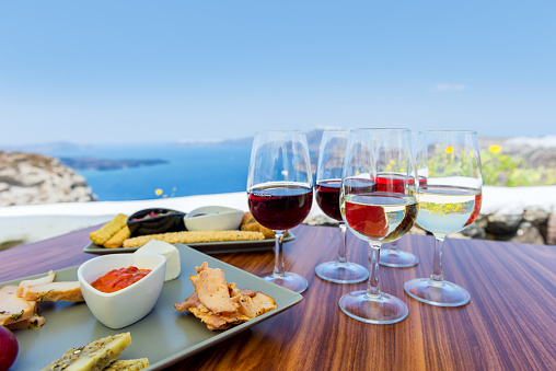 Horizontal color close-up image of greek appetizer. Tasting red, white and rose wine. Sea view in the background.