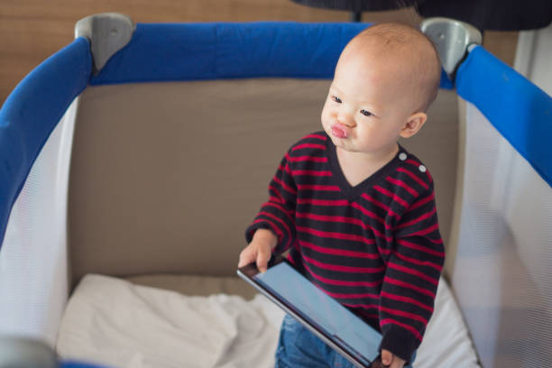 süße asiatische kleinkind baby junge stehend in krippe und tablet halten und lustiges gesicht - phone cradle stock-fotos und bilder