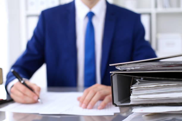 istock Binders with papers are waiting to be processed with businessman back in blur. Accounting planning budget, audit, insurance  and business concept 697288714
