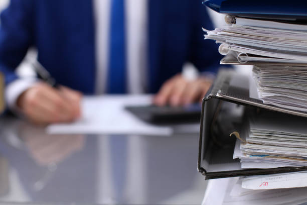 istock Binders with papers are waiting to be processed with businessman back in blur. Accounting planning budget, audit, insurance  and business concept 697288938