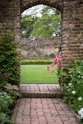 Archway in old English country garden landcape in Spring with tulips and border plants