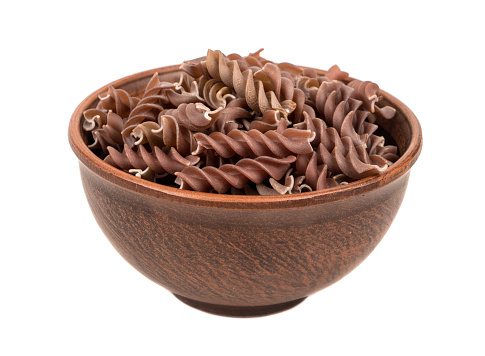 Uncooked pasta fussili in a large bowl on white background