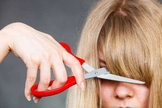 Woman cutting her fringe. Little look change concept. Young blonde woman cutting down shearing her fringe short front hair. Girl using big scissors. bangs hair stock pictures, royalty-free photos & images