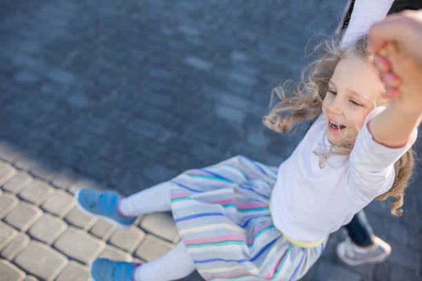 Little preschool girl swinging on parents hands