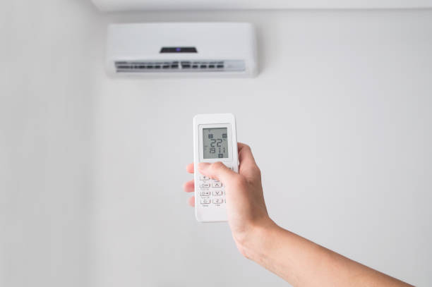 istock Hand holding remote control for air conditioner on white wall. 697372324