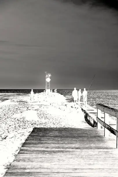 This solarized image depicts three men gathered around their fishing equipment on the Ocean City Jetty at dawn on while other tourist gather at the end of the jetty to watch birds and just look around.