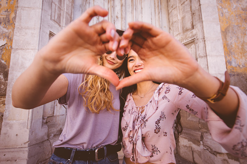 Teenage female hipster friends forming a heart with their hands in old city streets