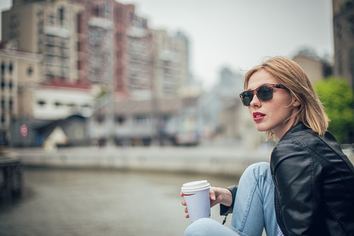 Beautiful woman sitting by the river holding cup of coffee