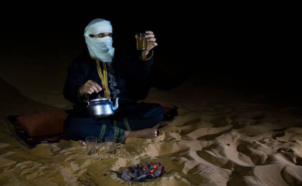 istock Man in traditional Tuareg outfit making tea in a desert 697434452