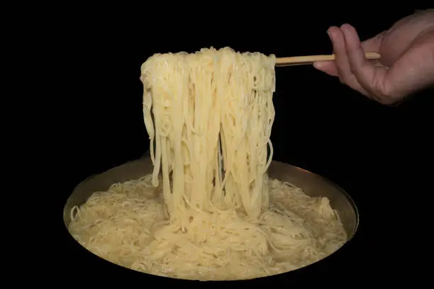 a hand holds chopsticks lifting noodles