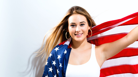 Happy young woman holding American flag on a white background