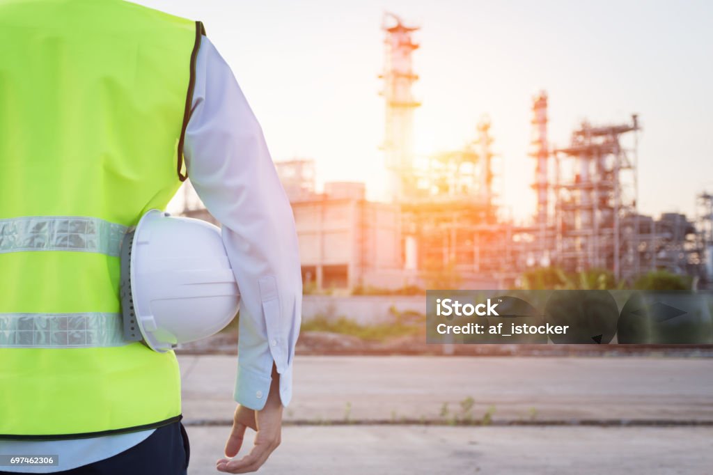 Homme de génie debout avec un casque de sécurité blanc près de raffinerie de pétrole - Photo de Chantier de construction libre de droits