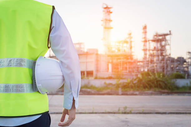 homme de génie debout avec un casque de sécurité blanc près de raffinerie de pétrole - raffinerie photos et images de collection