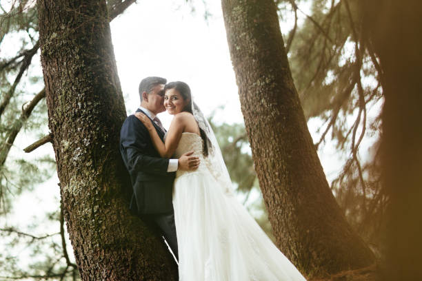 istock Latin bride with groom standing next to tree and smiling 697493590