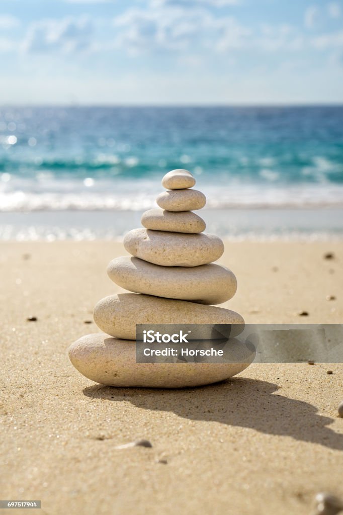 Stacked tower of balancing smooth pebbles. Stacked tower of balancing smooth stones on the sand of a tropical beach with the ocean behind symbolic of longevity, luck and happiness. Art Product Stock Photo