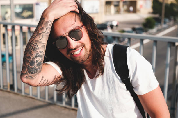 Stylish hipster model with long hair lifestyle in the street. Dressed in a white T-shirt and torn blue jeans in the city