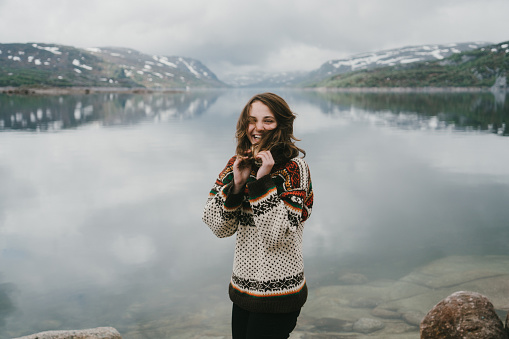 Woman in knitted sweater laughing near the  fjord in Norway