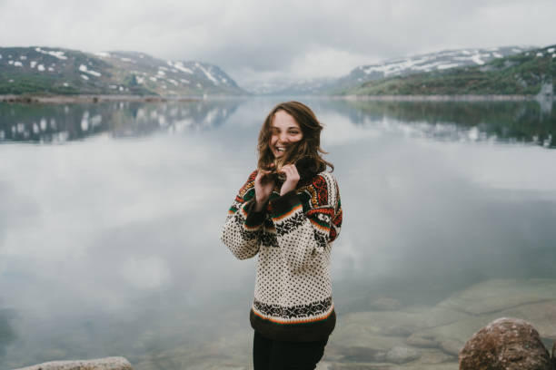 Woman in knitted sweater laughing near the  fjord in Norway Young Caucasian woman in knitted sweater  laughing near the  fjord in Norway lake scandinavia stock pictures, royalty-free photos & images