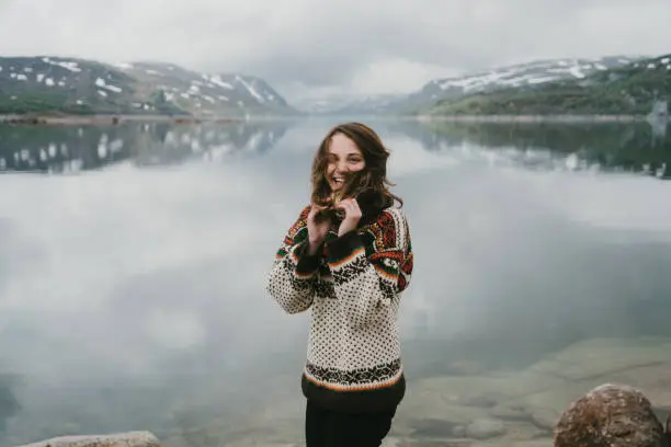 Young Caucasian woman in knitted sweater  laughing near the  fjord in Norway