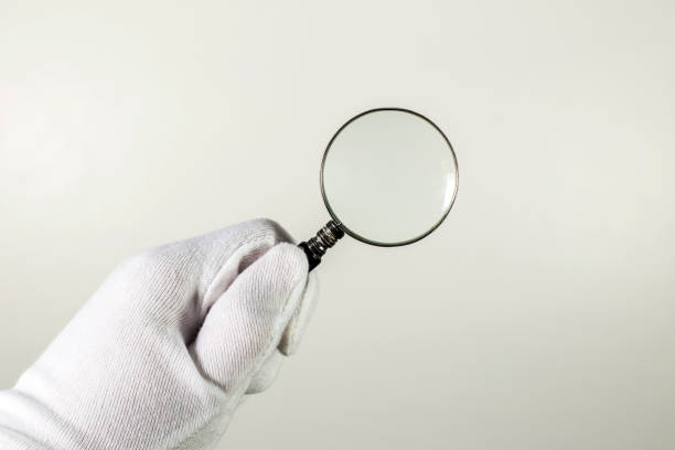 istock White glove holding magnifier on the gray background. 697547852