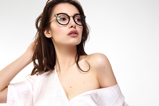 Female Eye wear. Attractive Brunette Girl With Natural Face Makeup In Transparent Glasses Frame. Beauty Woman Face. Portrait Of Beautiful Sexy Young Female With Perfect Makeup, Soft Fresh Healthy Skin And Thick Long Black Eyelashes. Glamorous Girl On Grey Background. High Resolution