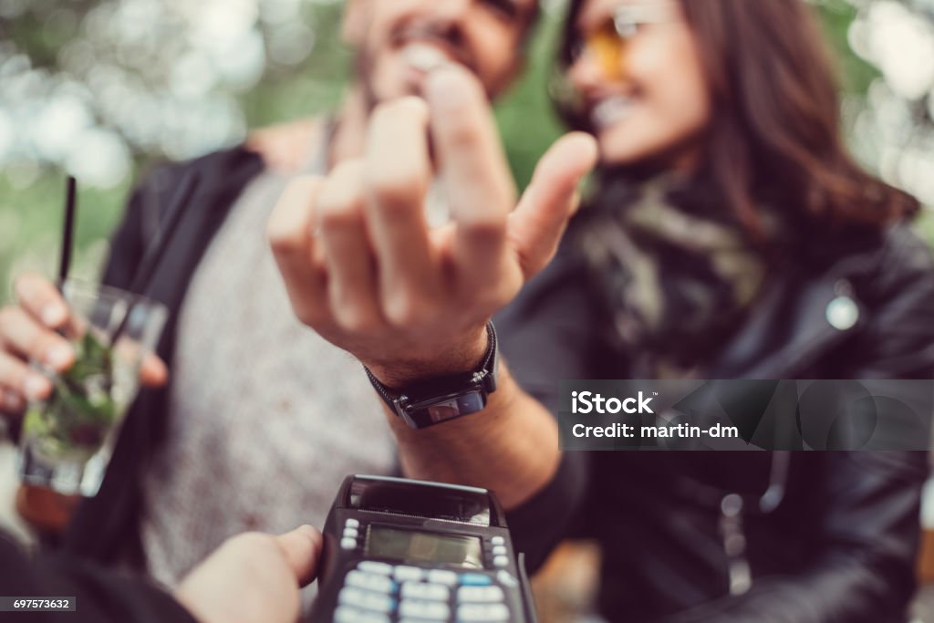 Man at cafe paying contactless with smartwatch Young couple paying contactless with smartwatch ++++ Note for the inspector: Credit card on the smartwatch is fake and made especially for the photosession ++++ Paying Stock Photo