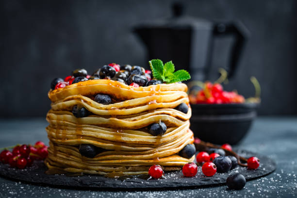 Pancakes with fresh berries and maple syrup on dark background, closeup