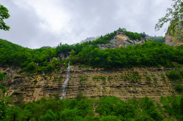 chute d’eau sur une montagne de rocher. fond d’écran paysage nuageux avec le vert de la forêt du caucase. gorge de guam - waterfall rock mountain bright photos et images de collection