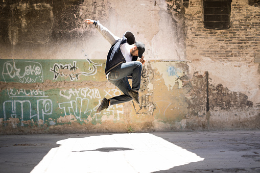 Good looking male hip hop dancer jumping and performing in an abandoned building with graffiti walls