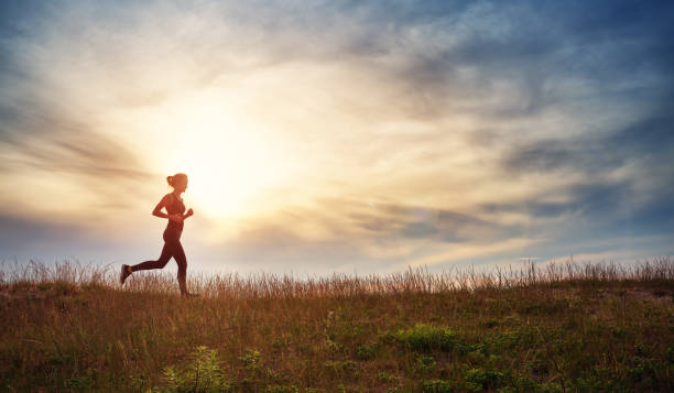 młoda kobieta biegająca po polu w pobliżu morza o zachodzie słońca - sun people jogging sunset zdjęcia i obrazy z banku zdjęć