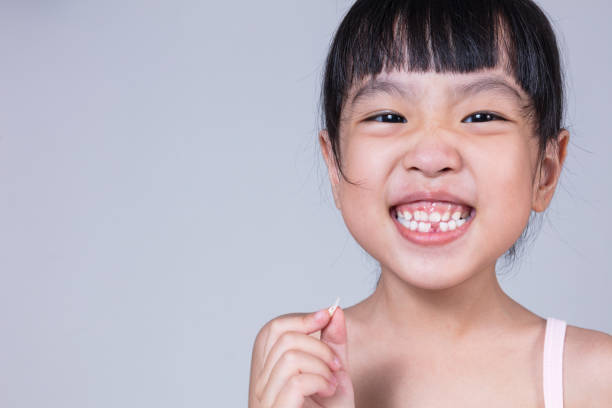 Asian Chinese little girl holding her missing tooth Asian Chinese little girl holding her missing tooth in isolated white background gap toothed photos stock pictures, royalty-free photos & images