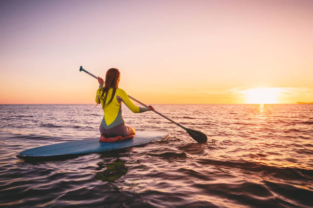 meisje op stand up paddle board, rustige zee met warme kleuren van de zonsondergang. ontspannen op de oceaan - paddle surfing stockfoto's en -beelden