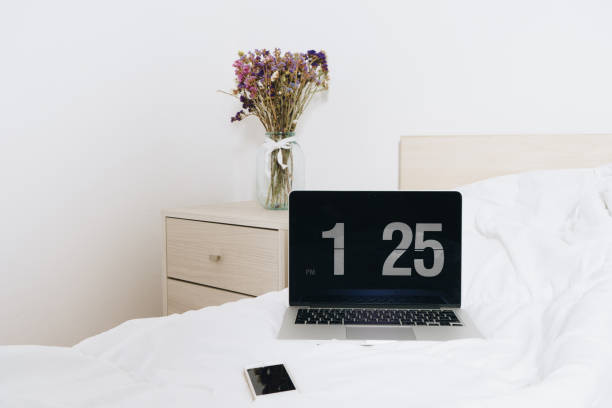 istock Flower on Table bedside in a light bedroom with lap top and mobile on bed 697675126