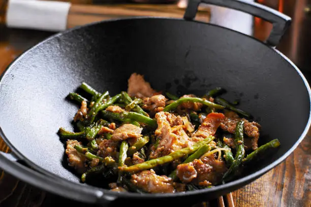 large cast iron wok with chicken and stringbean stirfry shot with selective focus