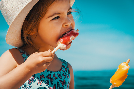 Little and cute girl eating ice cream on the beach on vacation