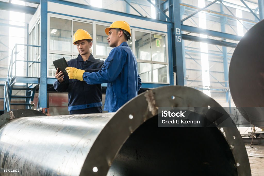 Experts checking information on tablet PC in a modern factory Asian experts checking information on tablet PC while supervising work in a modern factory Industry Stock Photo