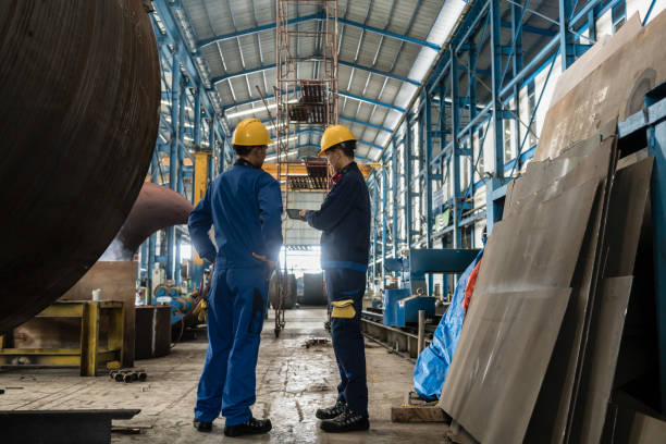 Two workers wearing yellow hard hat and blue uniform Two workers wearing yellow hard hat and blue uniform in the interior of an industrial hall manufacturing occupation stock pictures, royalty-free photos & images