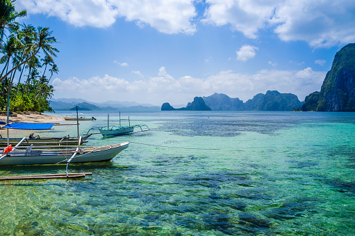 Banca boats in clear water at sandy beach in El Nido, Philippines.