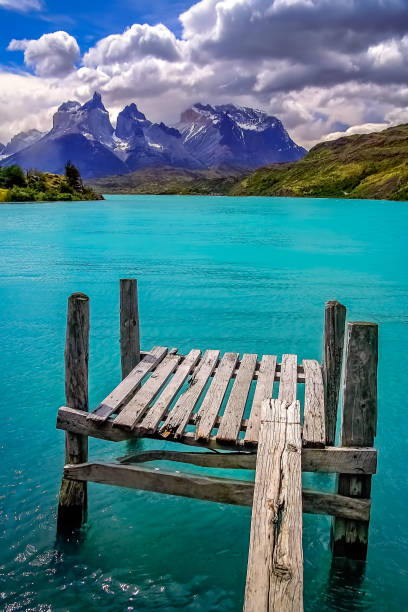A fiery sunset paints the skies over Lake Azul in Torres del Paine, Patagonia, with wooden posts and a canoe adding serene foreground interest.