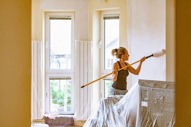 istock Young woman painting wall with telescopic roller 697763442
