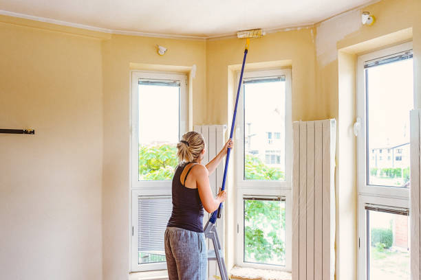 istock Young woman painting ceiling with telescopic roller 697766436