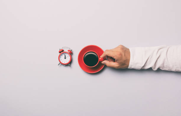 istock Man holding red cup of coffee near alarm clock 697770898