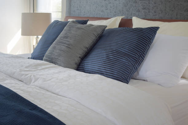 istock Gray and deep blue pillows on bed and white reading lamp in background 697801072