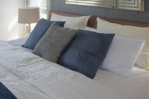 istock Gray and deep blue pillows on bed and white reading lamp in background 697802188